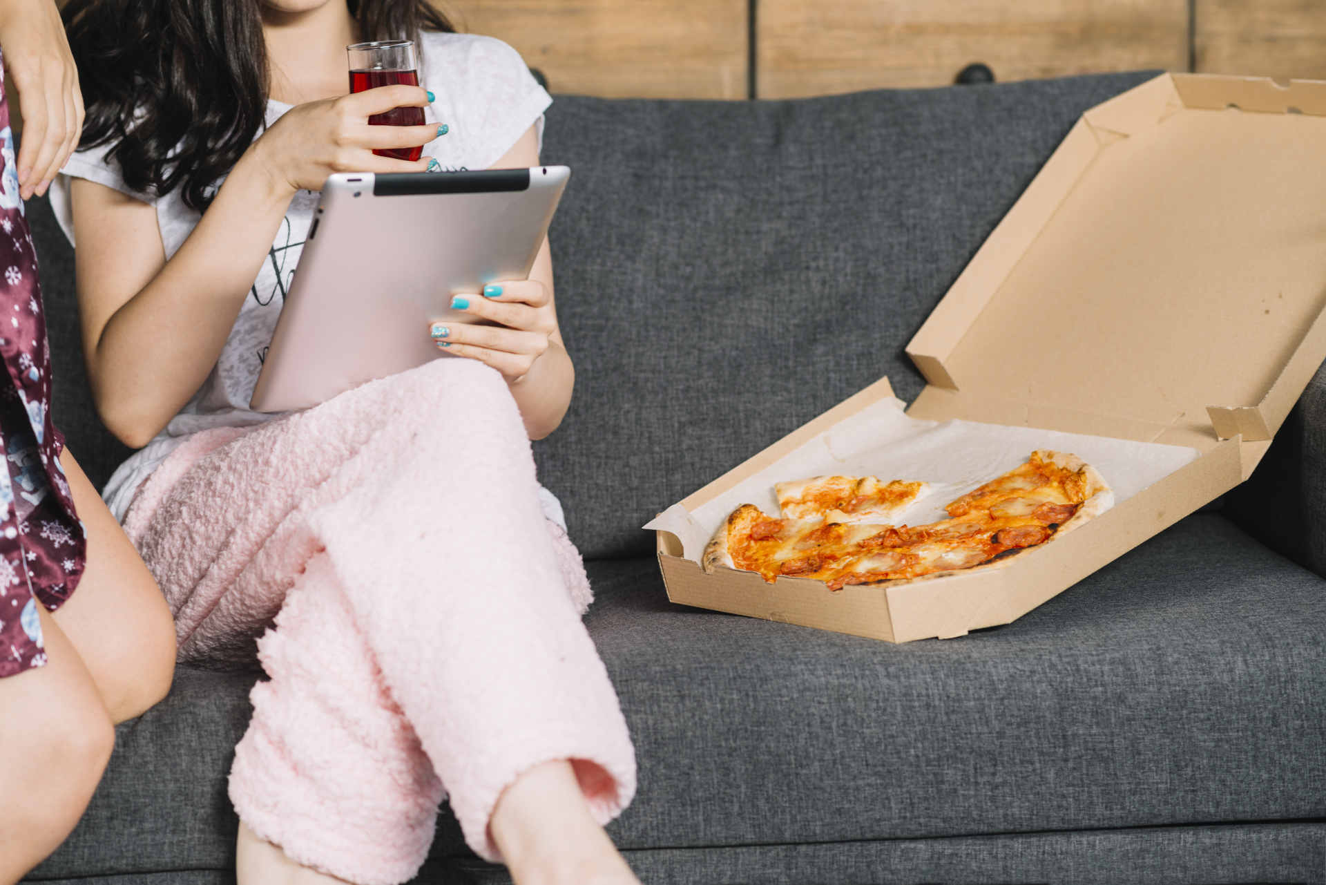two women using digital tablet sitting sofa with pizza